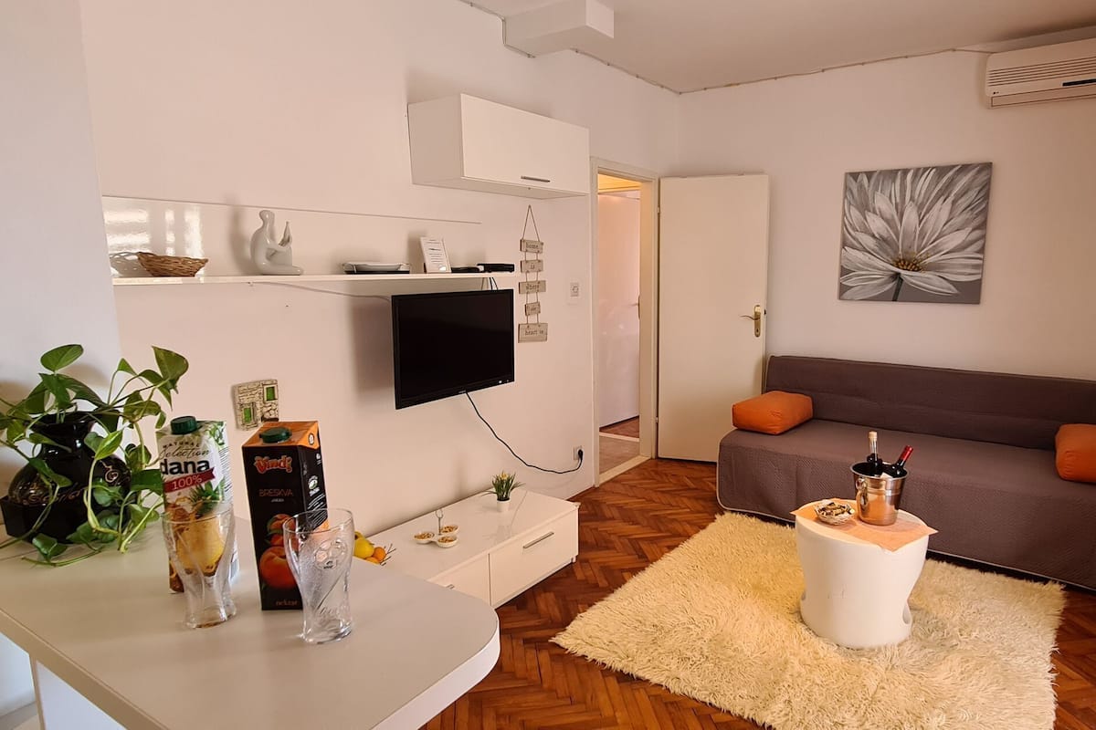 A modern living room with a flat-screen TV, a sofa, a coffee table, and a small plant on a white table.
