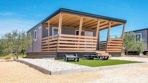 A modern, single-story cabin with a covered porch, a small patio, and a gravel driveway. - Mobile Home Banovi Dvori II (Tisno)