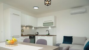 A modern kitchen with white cabinets, a wooden countertop, and a dining area with a table and chairs. - House Natalija (Primosten)
