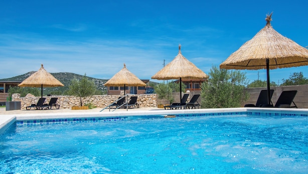 A swimming pool with lounge chairs and thatched umbrellas, surrounded by stone walls and a clear blue sky. - Mobile Home Banovi Dvori III (Tisno)