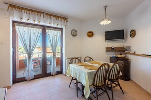A dining area with a table set for four, a television mounted on the wall, and a view through the glass doors to the outside. - Apartments Mavero (Medulin)