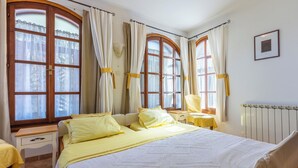 Een slaapkamer met een groot bed, twee nachtkastjes, een stoel en een raam met gordijnen.