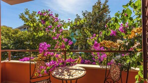 Een balkon met een ronde tafel en twee stoelen, omringd door felroze bougainvillea bloemen.