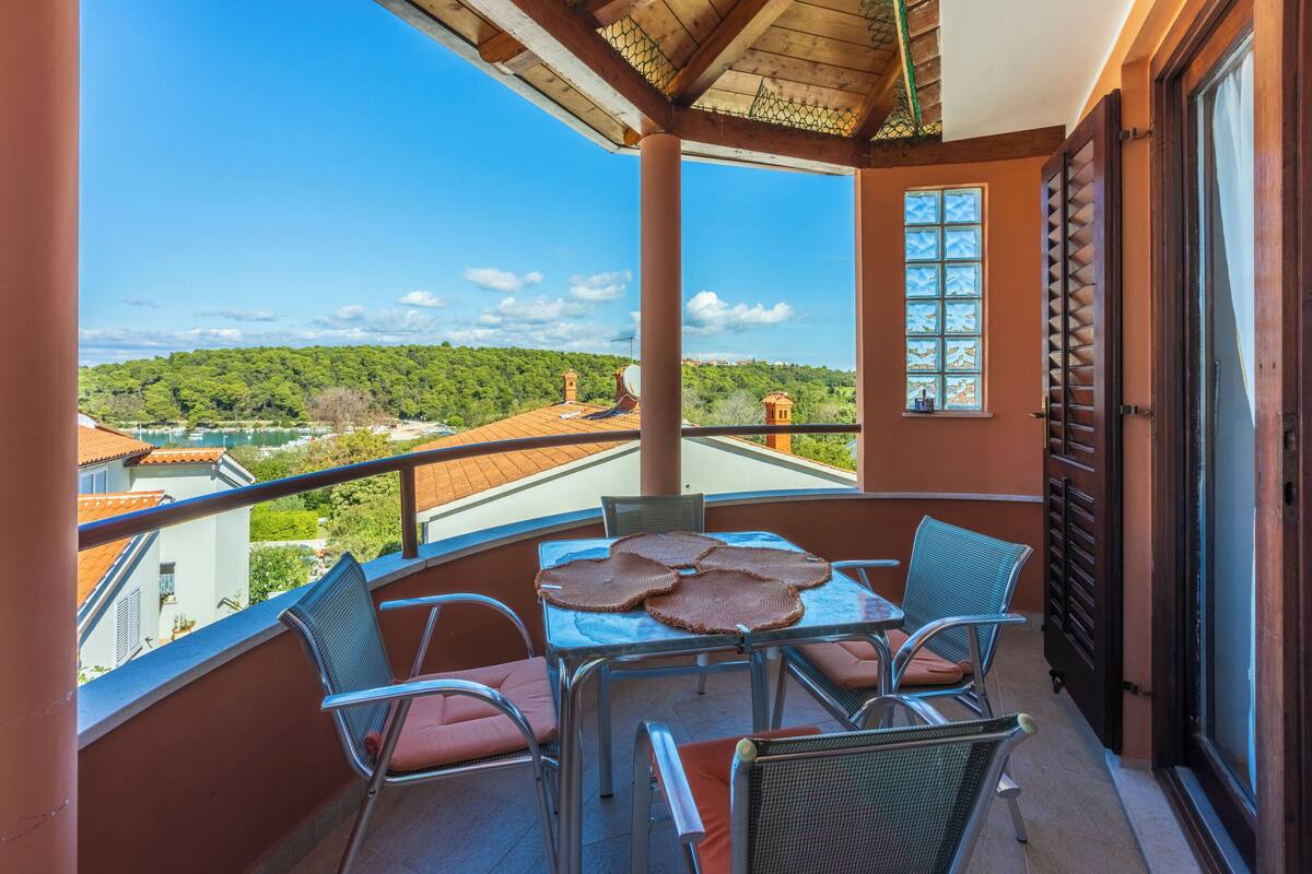 Un balcon avec une table et des chaises, une vue sur un paysage verdoyant et une porte en bois.