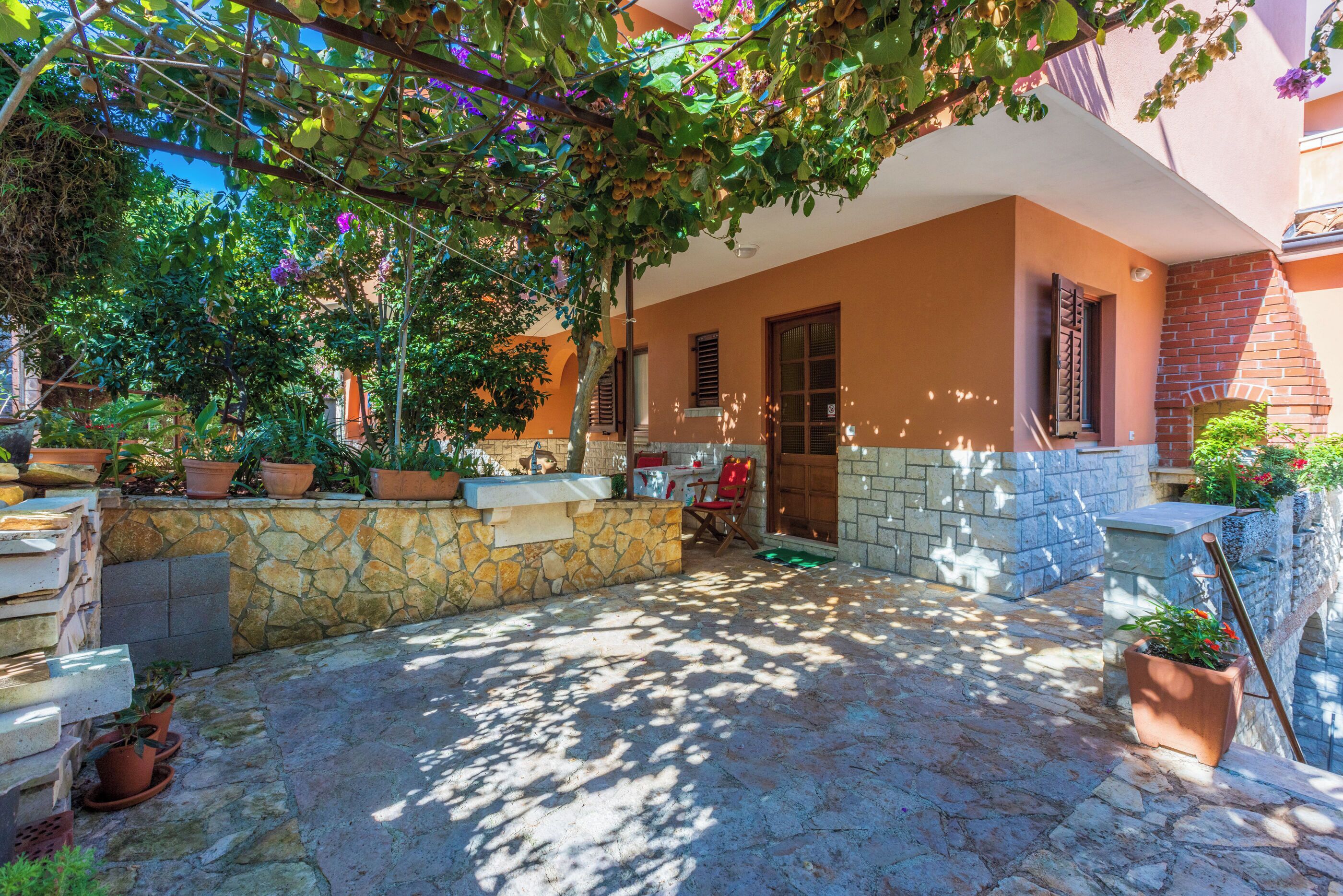 A courtyard with stone flooring, potted plants, and a brick wall.