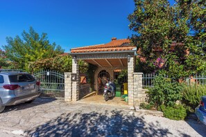 Un ingresso ad arco in pietra a una proprietà con tetto in tegole, una motocicletta parcheggiata e un'auto.