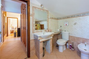 A bathroom with a sink, toilet, and bidet. There is a mirror above the sink, and a trash can is visible. The bathroom has tiled walls and floor. - Apartments Mavero (Medulin)
