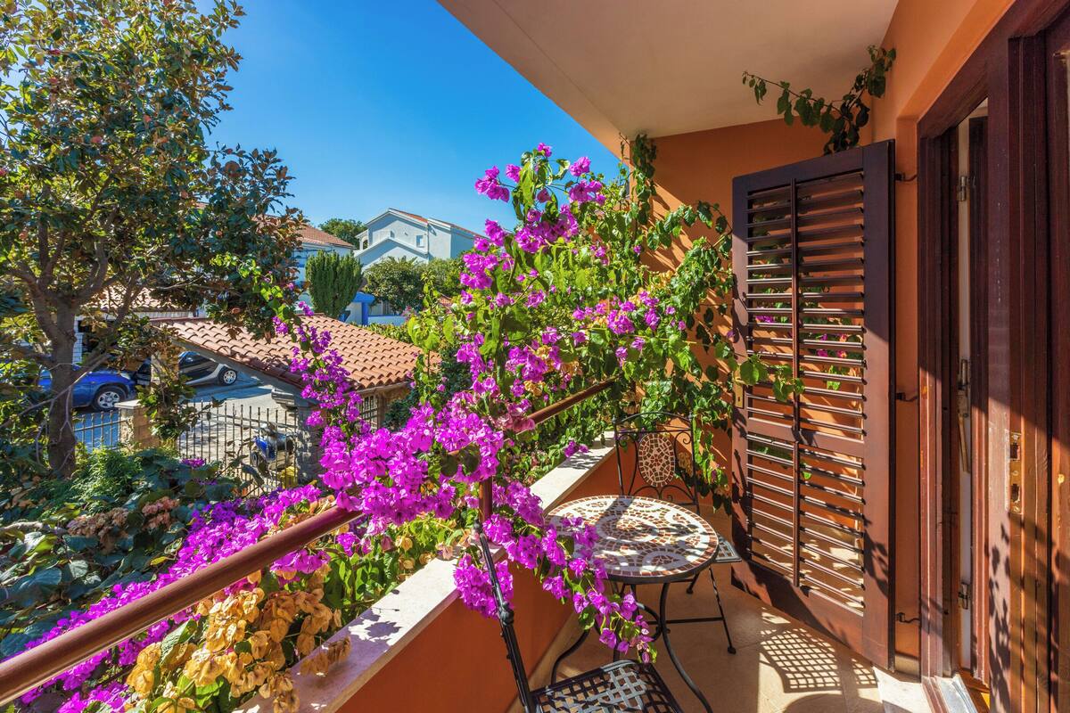 Un balcon agrémenté d’une table et de chaises, entouré de magnifiques fleurs de bougainvillier d’un violet éclatant.
