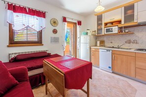 Una stanza compatta con un letto, un tavolino, angolo cottura e finestra con tende.