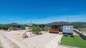 A row of cabins with a gravel driveway, a lawn, and a mountain backdrop. - Mobile Home Banovi Dvori IV (Tisno)