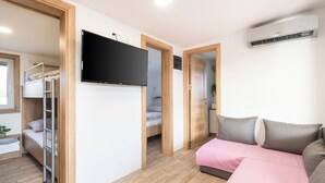 A room with a bunk bed, a sofa bed, a flat-screen TV, and an air conditioning unit. - Mobile Home Banovi Dvori IV (Tisno)