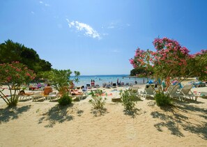 A beach with sun loungers, umbrellas, and people relaxing. - Apartment Alice (Pakostane)