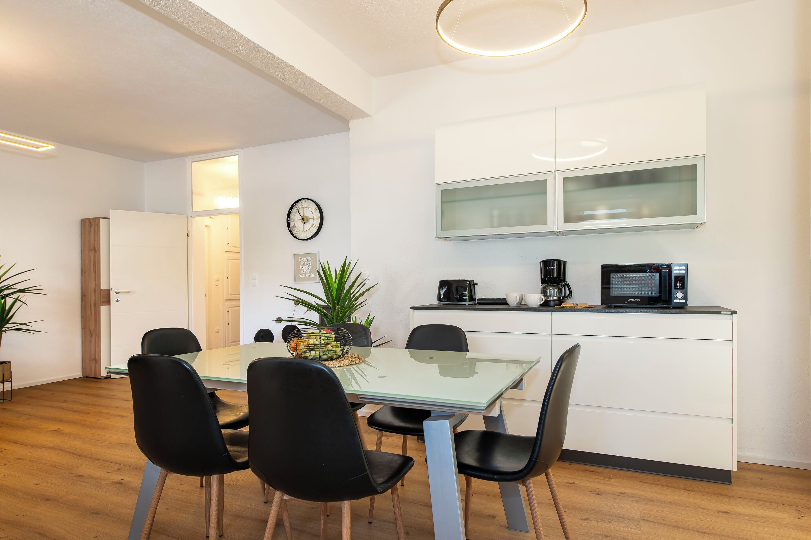 A modern kitchen with a glass-top dining table, black chairs, and white cabinetry.