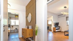 Una sala de estar moderna con piso de madera, un mueble de madera, un jarrón blanco con una planta y un televisor sobre un pedestal de madera.