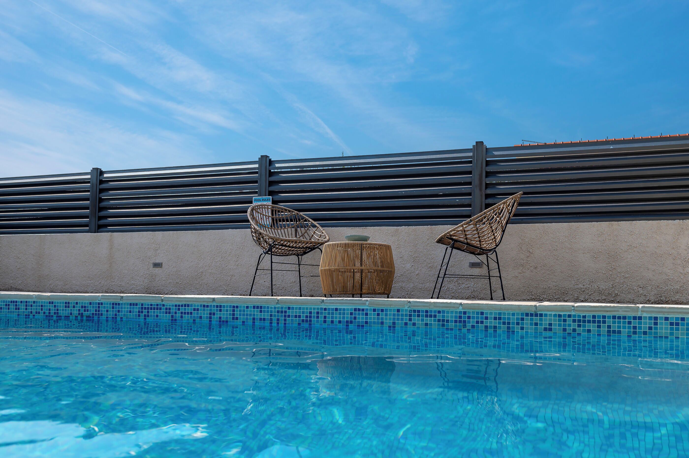 Une piscine avec deux fauteuils en osier et un tabouret en bois.