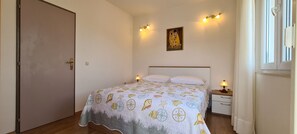 A bedroom with a bed, bedside lamps, a nightstand, a door, and a painting on the wall. - Apartment Sea View (Jelsa)