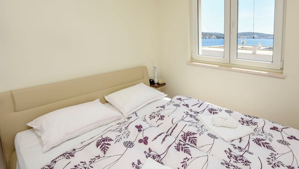Een bed met een bloemenbedekking, een wit kussen en een nachtkastje met een lamp.