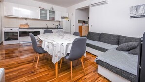 Een moderne keuken met witte kasten, een eettafel met een witte tafelkleed en een grijze bank.