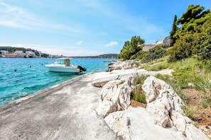 A coastal road with a boat docked on the water, rocky terrain, and a clear view of the sea. - Apartment Slavica (Rogoznica)