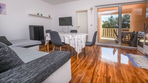 Een moderne woonkamer met een bank, een eettafel met stoelen, een flatscreen televisie en een glazen schuifdeur die leidt naar een buitenruimte met een barbecue.
