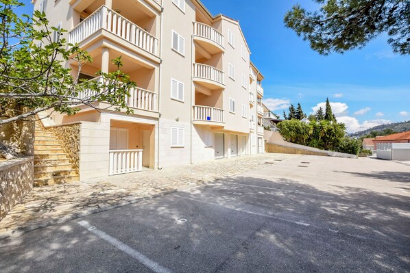 A multi-story residential building with balconies, a stone staircase, and a parking area. - Apartment Slavica (Rogoznica)