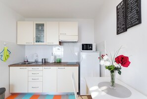 A modern kitchen with white cabinets, a microwave, and a vase with flowers on the counter. - House Cvetko (Lovran)