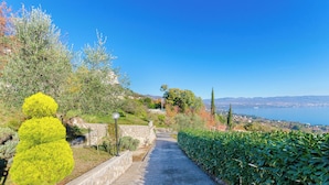 A paved pathway flanked by greenery and stone walls, leading to a scenic overlook with a view of the sea and distant hills. - House Cvetko (Lovran)