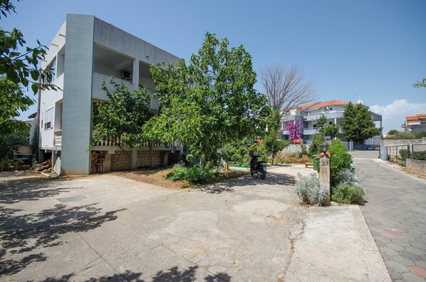 A residential building with a concrete facade, a paved driveway, and a small tree in the foreground. - Apartment Lily (Vodice)