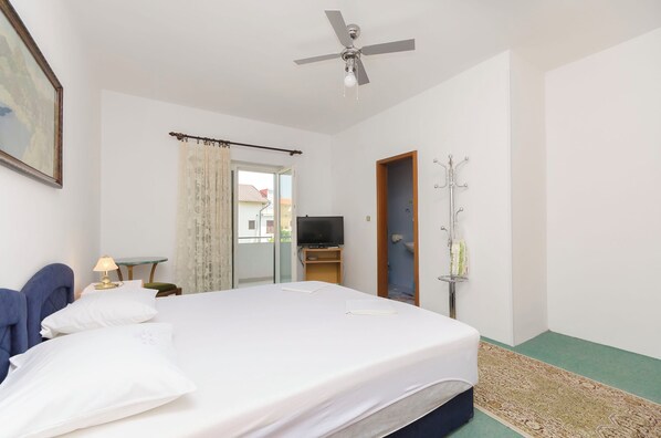 Una camera d'albergo con un letto, una ventola a soffitto, una televisione, un tavolino e una finestra con tende.