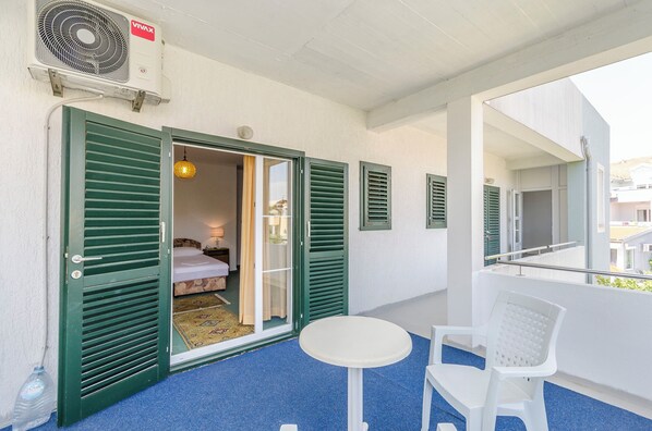 A balcony with a white table and chairs, a fan, and a room with a bed and curtains. - Apartment Lily (Vodice)