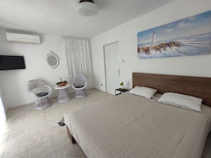 A bedroom with a large bed, two wicker chairs, a small table with a basket, a painting of a lighthouse, and an air conditioning unit. - House House Povile (Novi Vinodolski)