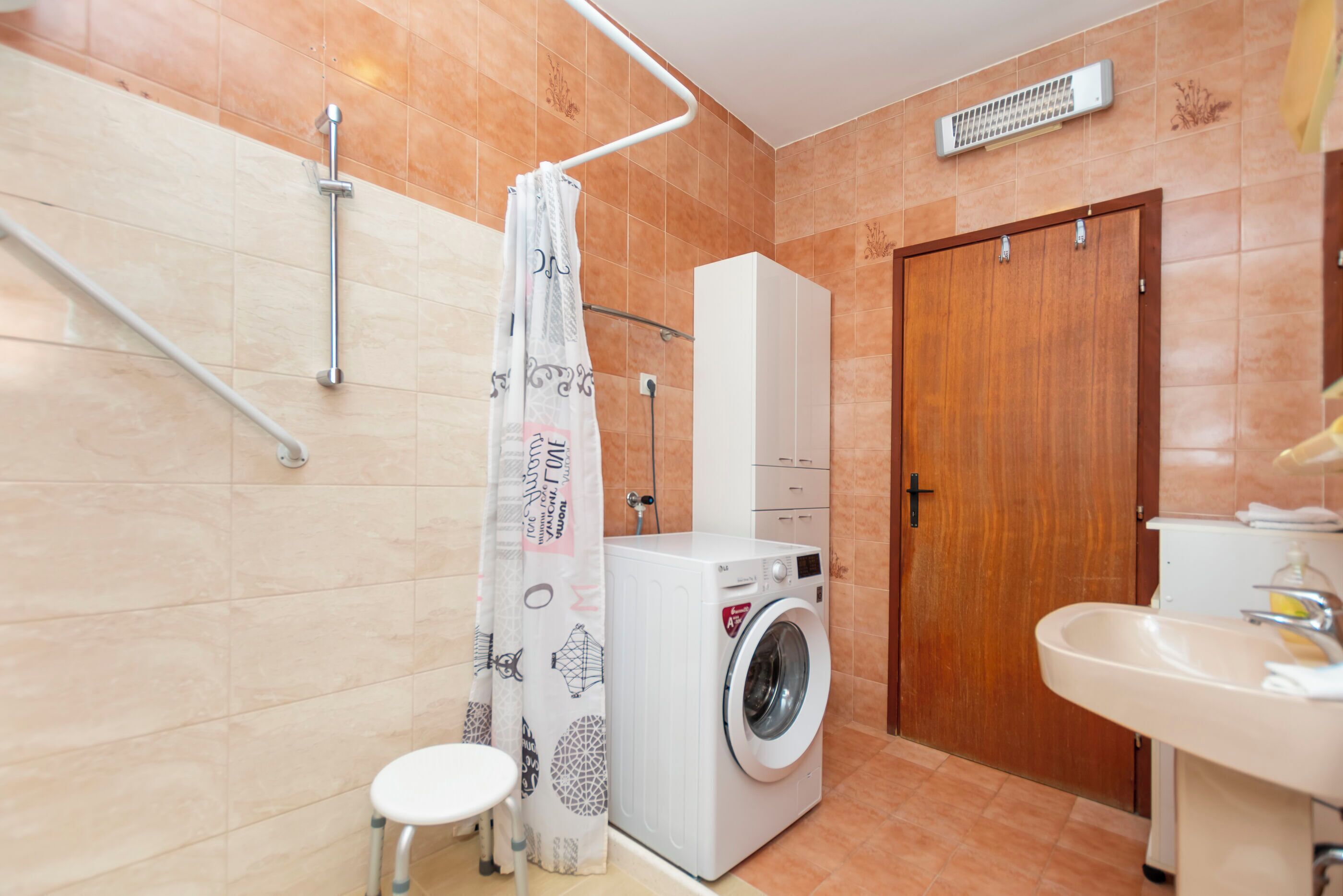 A bathroom with a washing machine, a sink, a shower with a curtain, and a wooden door.