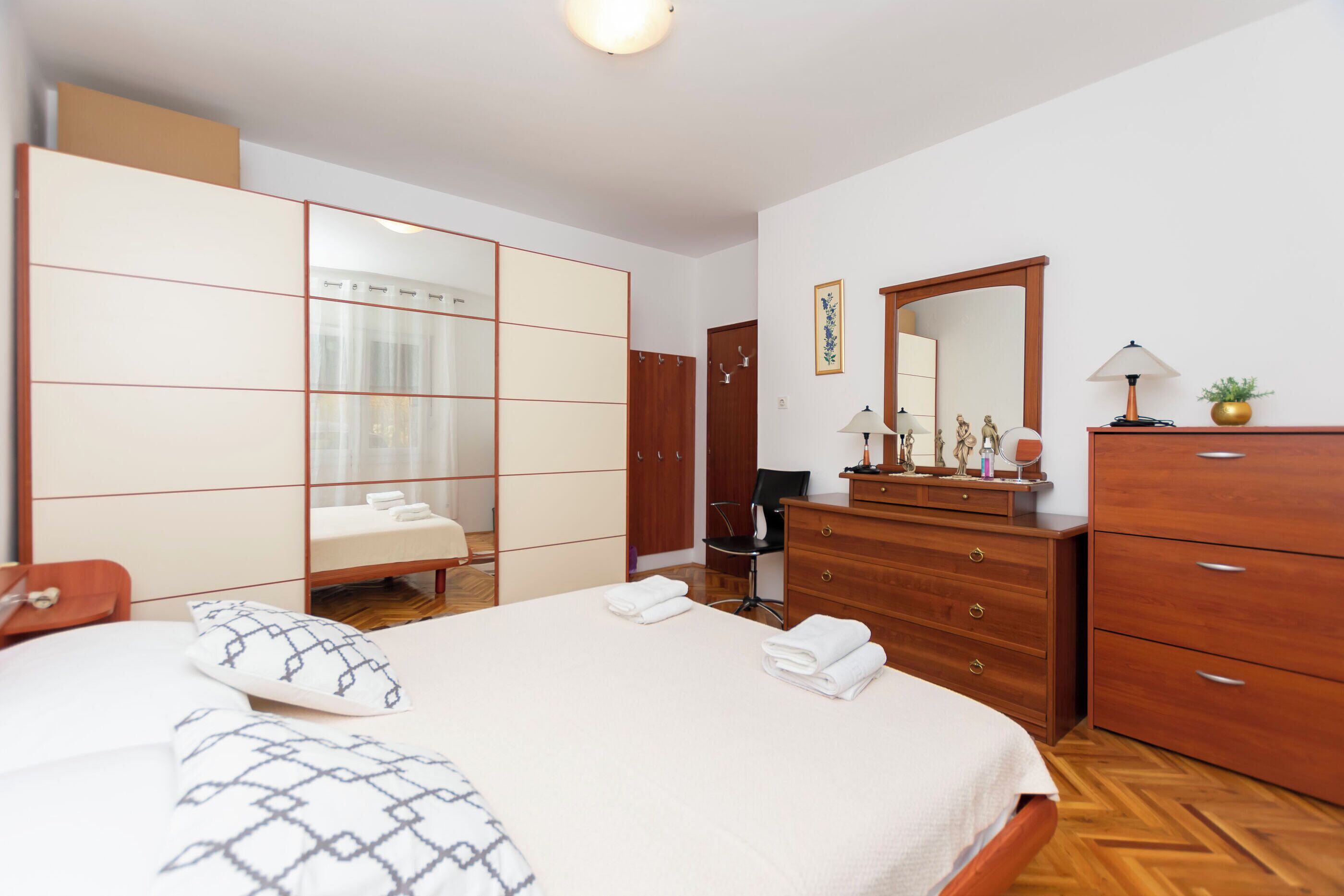 A hotel room with a bed, a wooden dresser, a mirror, and a wardrobe.