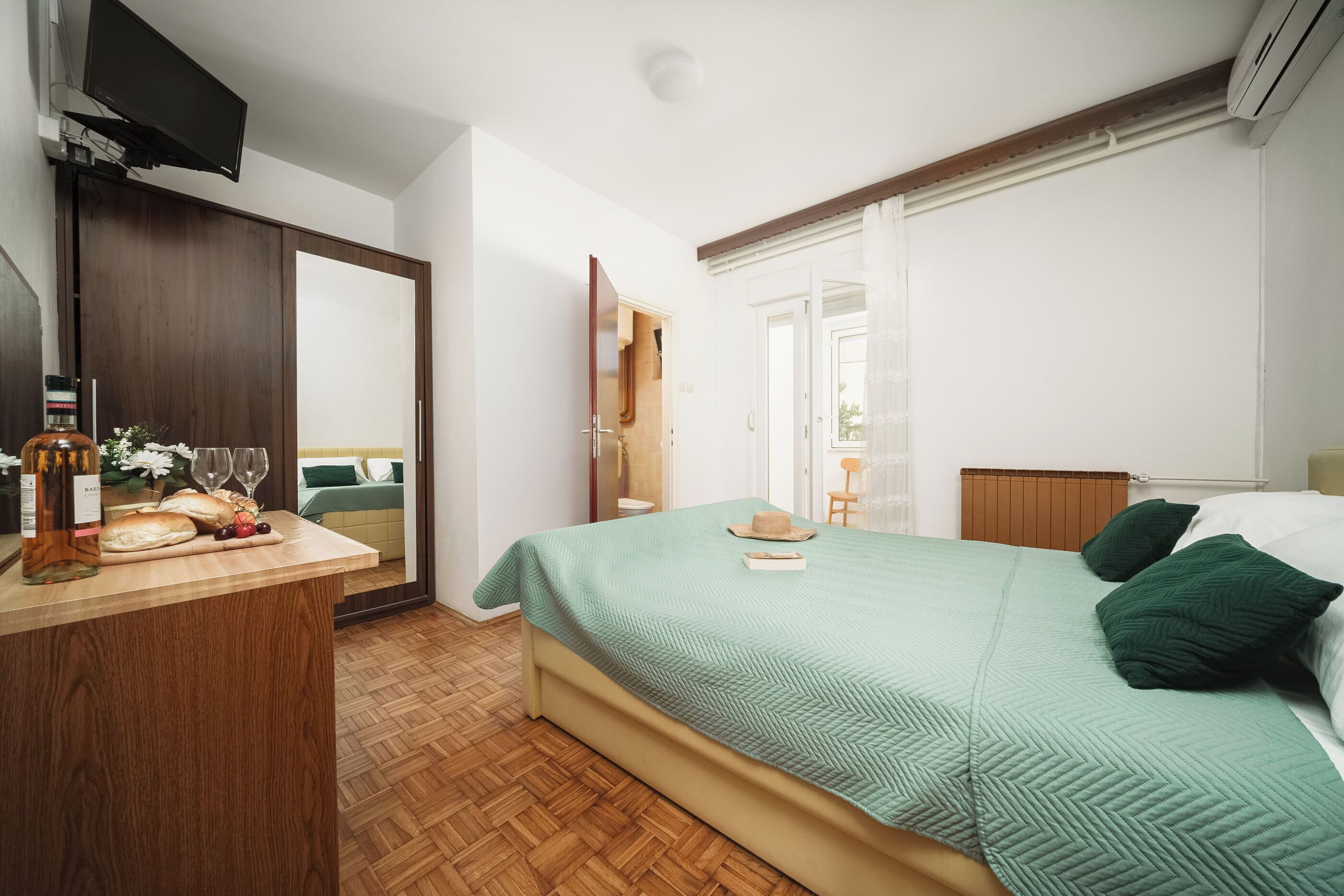 Um quarto com uma cama, cômoda de madeira, televisão e janela com cortinas.