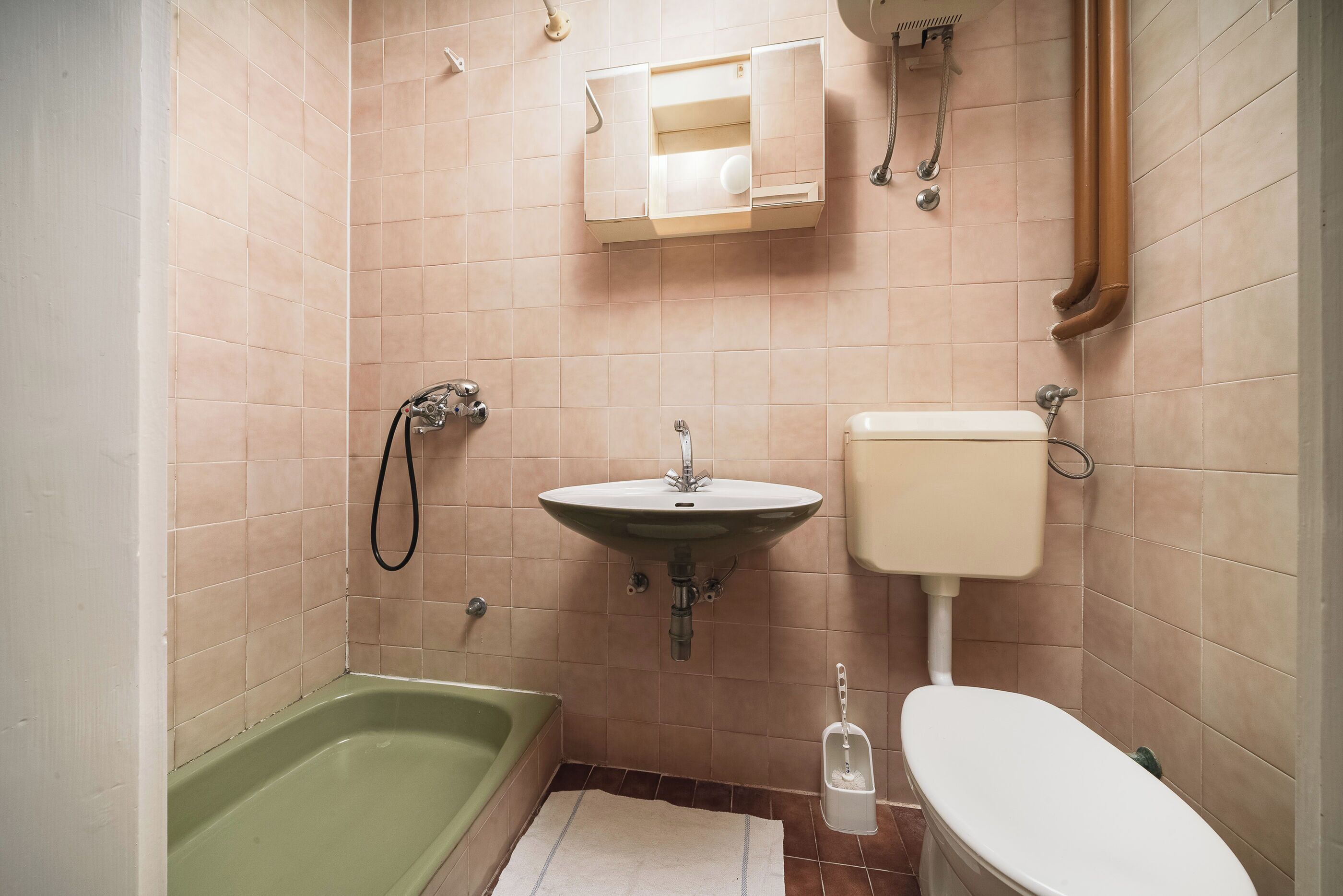 A bathroom with a green bathtub, a sink, a toilet, and a towel rack.