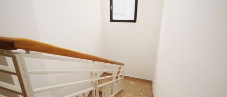 A staircase with a wooden handrail and white railings, leading to a room with a small window and a hanging light fixture.