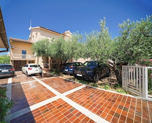 A residential area with parked cars, a tiled patio, and a building with a balcony. - Apartment and Rooms Mrkovic Top Lokacija i Parking (Vodice)