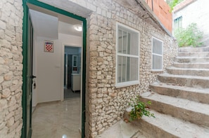 A stone building with a green door, a window, and a staircase leading to an upper level. - Apartment Roko (Omis)