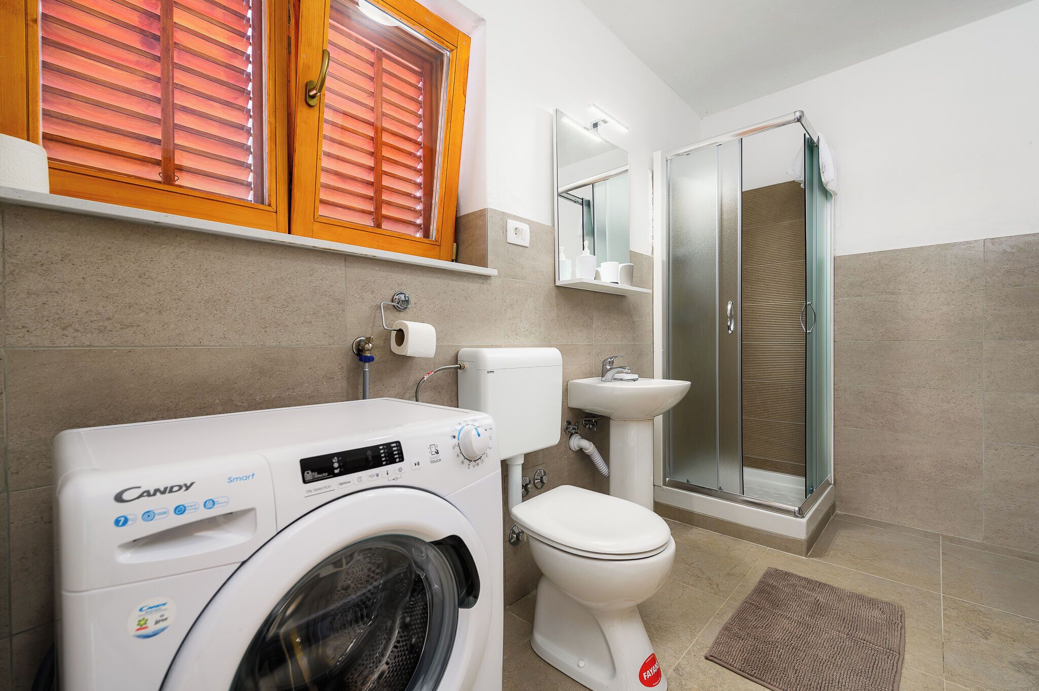 A modern bathroom with a washing machine, toilet, and glass shower enclosure.