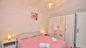 Ein Schlafzimmer mit rosa Bettdecke, einem weißen Kleiderschrank und Nachttischlampen.