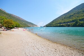 Een strand met kiezels, enkele mensen en een boot in de verte.