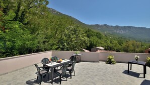 Eine Dachterrasse mit Esstisch und Stühlen, umgeben von üppigem Grün und Bergen im Hintergrund.
