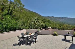 A rooftop terrace with a dining table and chairs, surrounded by lush greenery and mountains in the background. - House Carlo (Krsan)