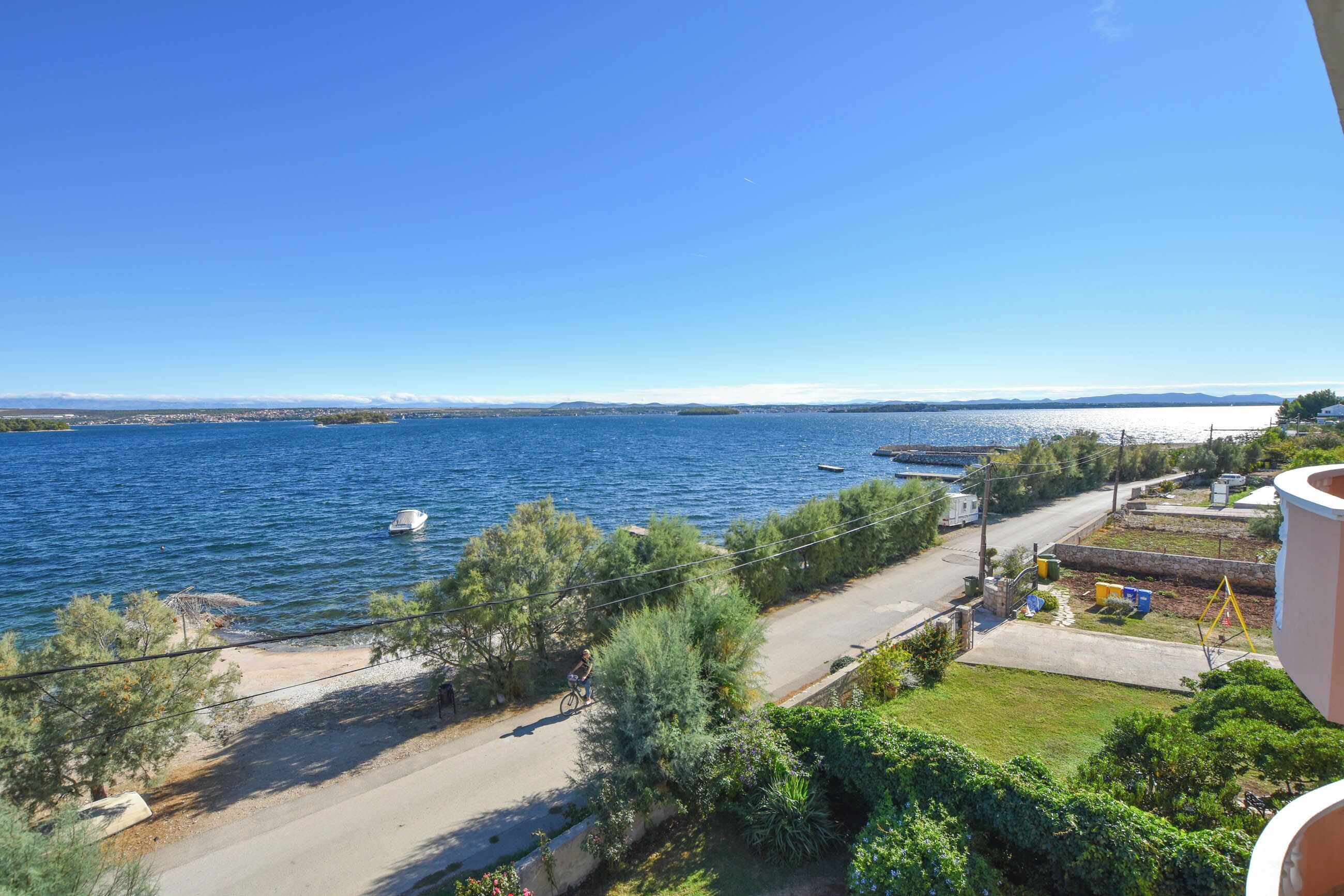 A coastal view with a road, greenery, and boats on the water.