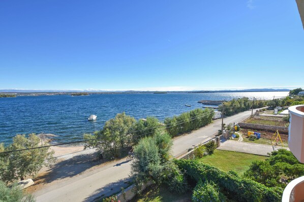 A coastal view with a road, greenery, and boats on the water. - Apartments Anita (Tkon)