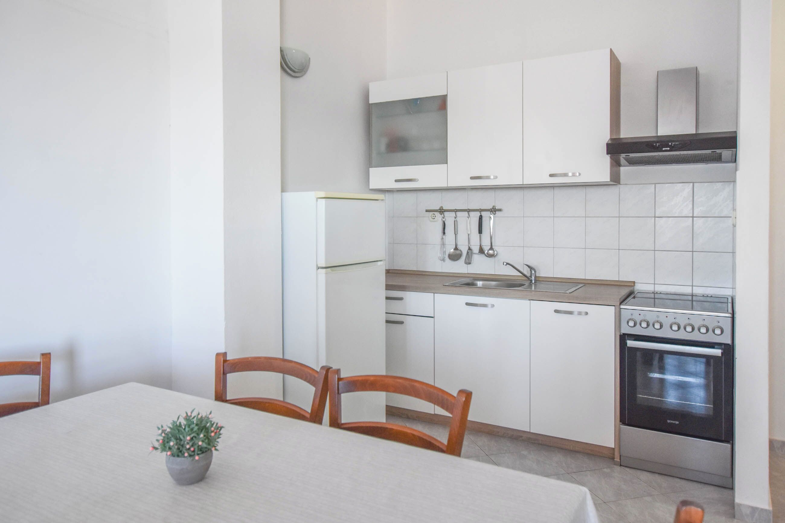 A compact kitchen with white cabinets, a built-in oven, and a small dining area with a table and chairs.