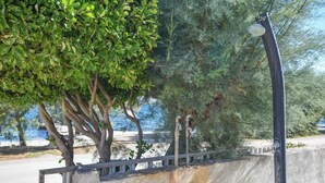 A coastal road with a metal railing, trees, and a clear view of the sea. - Apartments Anita (Tkon)