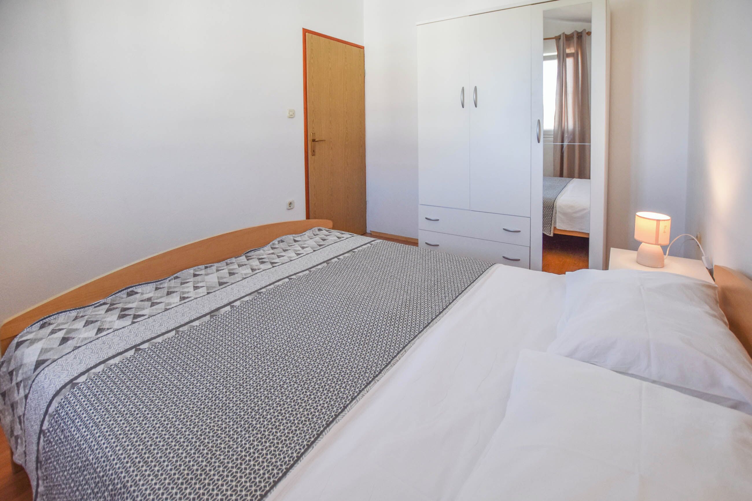 A bedroom with a bed, a wardrobe, a bedside table with a lamp, and a door leading to a bathroom.
