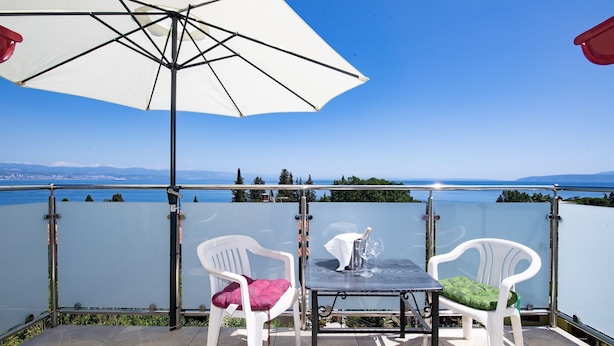 A terrace with a table and two chairs, overlooking a body of water and distant land. - Apartments Villa Anna (Opatija)