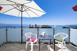 A terrace with a table and two chairs, overlooking a body of water and distant land. - Apartments Villa Anna (Opatija)